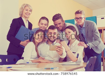 Positive students of different age doing group selfie on smartphone in classroom