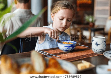 Adorable little girl eating cereal with milk for breakfast in restaurant