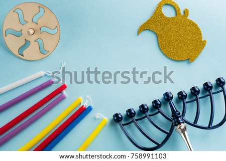 Image of jewish holiday Hanukkah with wooden dreidels (spinning top) , candles, menora (traditional Candelabra) , children's stickers glitter craft- jug of Chanukah on blue background.