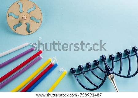 Image of jewish holiday Hanukkah with wooden dreidels (spinning top) , candles, menora (traditional Candelabra) , children's stickers glitter craft- jug of Chanukah and candles on blue background.