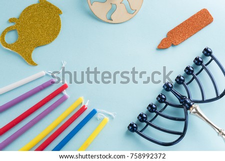 Image of jewish holiday Hanukkah with wooden dreidels (spinning top) , candles, menora (traditional Candelabra) , children's stickers glitter craft- jug of Chanukah and candles on blue background.