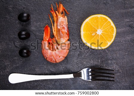 On the table is royal prawn, slice of lemon, a few olives and a fork.