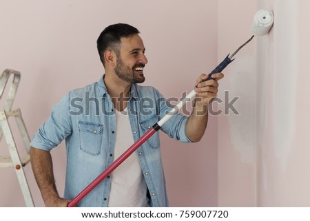 Handsome man is painting the house with a roller 