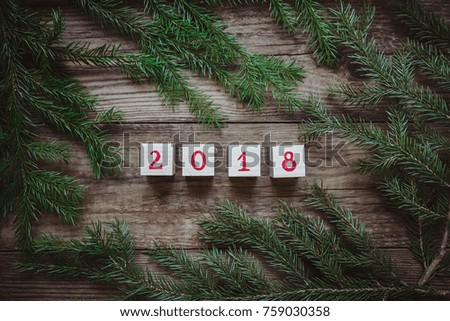Beautiful picture with green Christmas tree branches and dices with the number 2018 on wooden background, top view