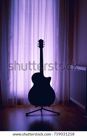 silhouette of an acoustic guitar on a light background of curtains and a large window of a house