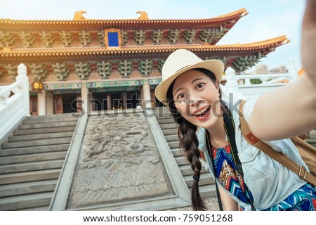 Happy Asian tourist taking a fun selfie at the famous tourist attraction in Beijing, China. Asia summer travel. Young woman taking mobile picture with smartphone at Temple.