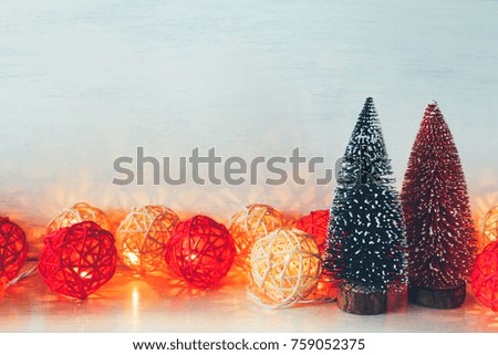 Miniature Christmas trees and New Year rattan light balls string on white wooden texture background. Copy space. Creative decoration concept for Christmas celebration and Holiday. Toned image.