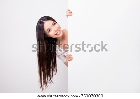 Copy space portrait of charming attractive girl hiding, standing behind empty white vertical wall isolated over white background
