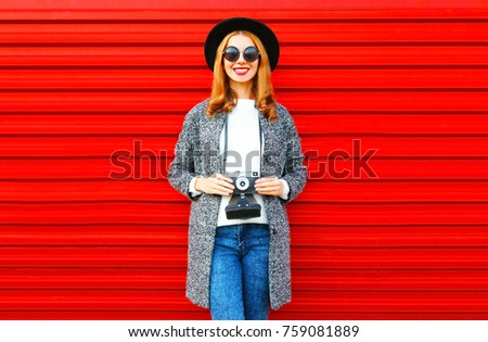 Fashion portrait pretty smiling woman holds retro camera on a red background