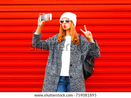 Fashion pretty cool young girl takes a picture self portrait on a smartphone on red background