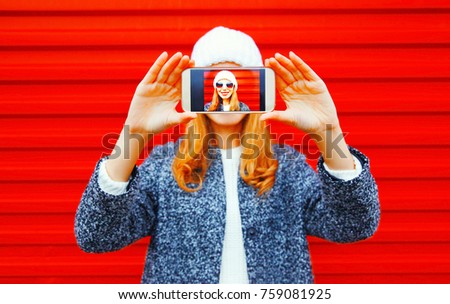 Fashion woman takes a picture self portrait on smartphone on a red background