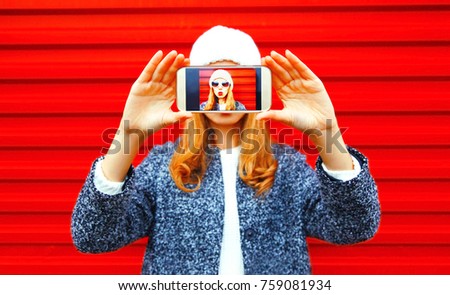 Fashion woman takes a picture self portrait on smartphone on red background