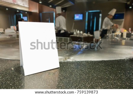 Mock up Menu frame on Table in Bar restaurant ,Stand for booklets with white sheets of paper acrylic tent card on cafeteria blurred ,Chef cooking in background.