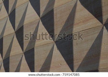 Concrete wall has geometric diamond pattern enhanced by low angle sun light.
