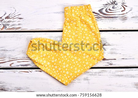 Baby-girl new folded trousers. Infant girl yellow printed leggings on white wooden background. Kids summer outfit. Baby flower print leggings.