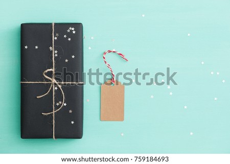 Top view on Christmas or birthday gift wrapped in black paper ready for  decorating with craft tag and twine. Present on turquoise background  with sparkling silver stars.