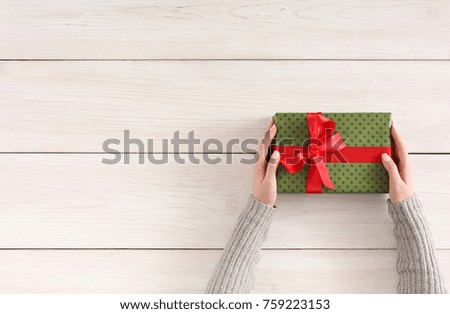 Gift wrapping background. Female hands holding handmade present box in green paper against white wooden table background. Bithday or christmas preparation concept, top view, copy space