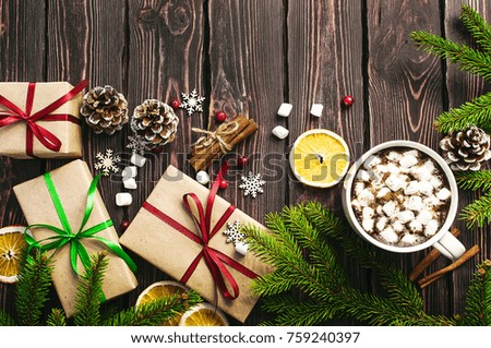 A cup of hot coffee with marshmallow, spruce branches, cones, Christmas gifts, mugs of orange, snowflakes, cinnamon. Traditional festive decoration Christmas dark background top view.