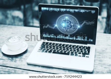 Close up of cafe table with digital bitcoin on laptop screen and coffee cup. Economy and cyberspace concept 