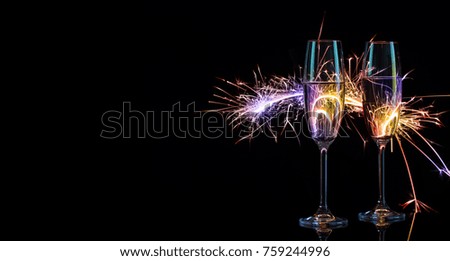 Two glasses of champagne in colorful Bengal lights. Black background. The concept of the celebration of the wedding and the new year. Copy space.