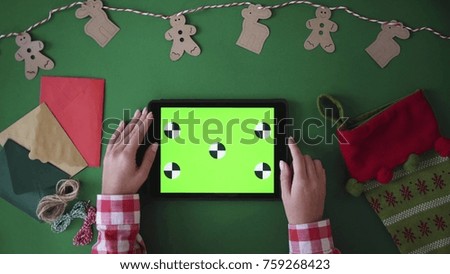 Woman hands scrolling, tapping, zooming on tablet with green screen. Christmas decoration on green table background. Chroma key. Top view. Tracking motion