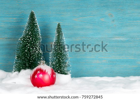 two evergreen fir trees and red ball, snowy christmas composition, blue wooden background, copy space