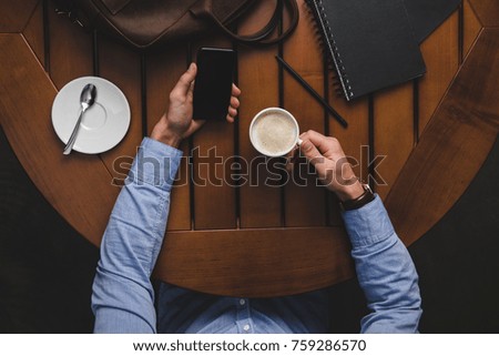 overhead view of man using smartphone and drinking coffee at wooden table
