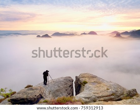 Photographer framing picture with eye on viewfinder. Photo enthusiast  enjoy work of fall nature on rocky summit. Dreamy landscape, misty sunrise in a beautiful valley below