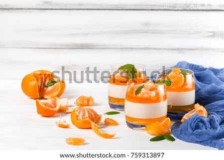 Creamy panna cotta with orange jelly in beautiful glasses and fresh ripe mandarin with blue textile on white wooden background. Closeup photography of delicious dessert.