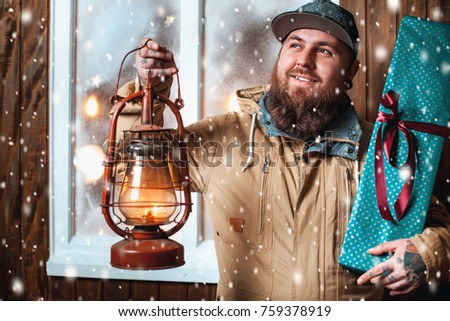Christmas night, snow falling, funny man with a beard and with gifts in hand and flashlight at the window. Winter background
