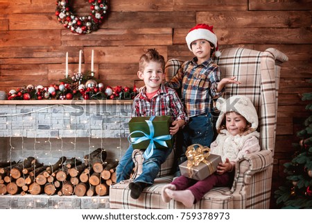 Beautiful children playing with gifts in hand on the armchair in a Christmas interior with Christmas tree and fireplace. The concept of a family holiday