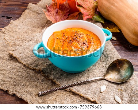 Photo on top of orange pumpkin soup in saucepan, spoon, autumn leaves