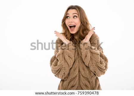 Picture of young surprised excited lady dressed in warm sweater standing isolated over white wall background. Looking aside.