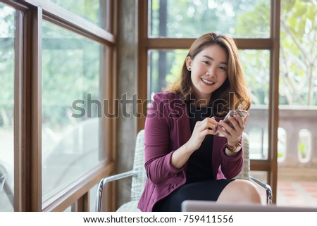 Smiling Business woman working in office with documents,Happy Asian businesswoman using phone sitting on chair at modern home studio.Concept of young people working mobile devices,contact to costumer