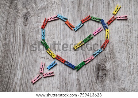 Composition heart pierced by an arrow made of wooden clothespins on a wooden background.
