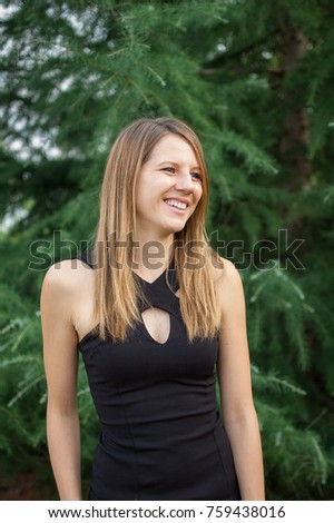 Outdoors Portrait of Attractive Smiling Woman in Black Shirt near Spruce Tree During Summer Time.