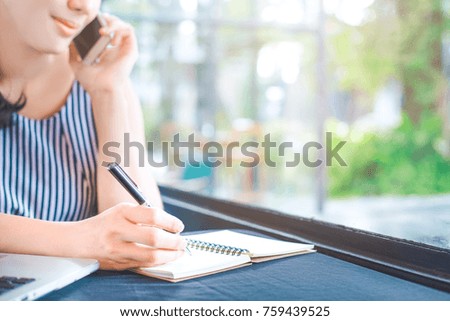 Business woman writing on notepad with a pen and talking on the phone in the office.