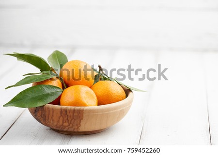 Fresh ripe tangerines or mandarins with leaves in a wooden bowl on white wooden background, copy space