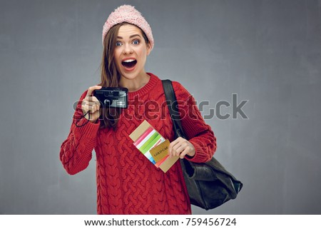 Happy surprising woman holding camera, credit card with passport and tickets. Gray wall back.