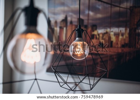 Close up two modern tungsten lamps in kitchen. White wall and with a big picture of New York and Brooklyn Bridge on the background. Orange warm light.