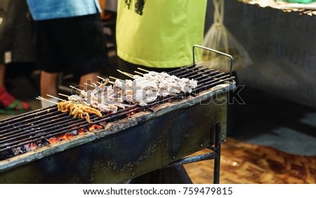 Grilled octopus on bamboo sticks placed on charcoal stove.