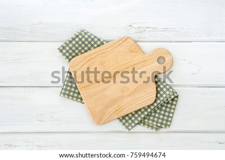 Wooden cutting board on napkin placed on white wooden table ,top view or overhead shot , food menu card or recipes background concept Royalty-Free Stock Photo #759494674