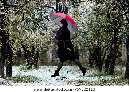 Adult girl with red umbrella in park while snow and rain.