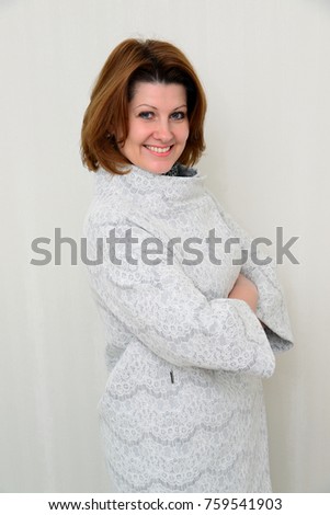 Woman in white lace coat stands against the wall background