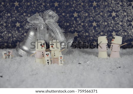 Christmas photography picture created using marshmallows shaped as snowman with iced happy smile and standing in snow with silver color bell decoration and star pattern background 
