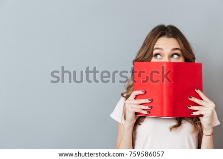 Portrait of a pretty young girl hiding behind an open book and looking away isolated over gray wall background Royalty-Free Stock Photo #759586057