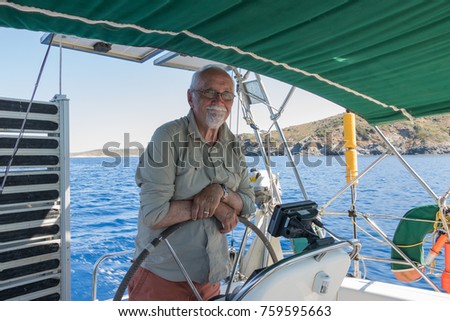 Old man holds a steering wheel of a boat and happy smiling. It`s a pleasure sailing in a blue sea. Fulfill your dreams to be a captain & yachtsman. Concept: active elderly people. Royalty-Free Stock Photo #759595663