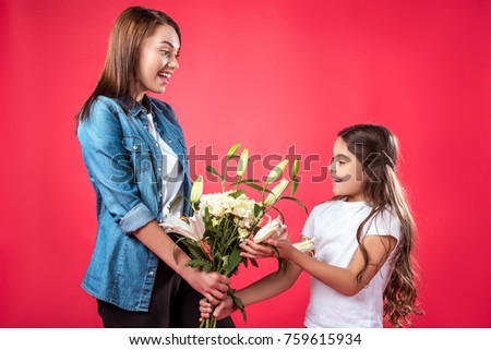 Mother presenting bouquet of flowers to daughter isolated on red