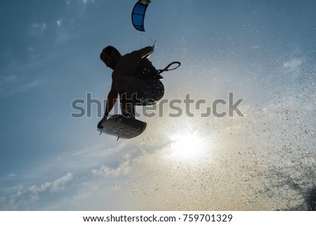 Silhouette of a Surfer flying in front of the sunset sun with splashing water in a corner of the photo