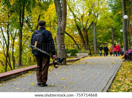 The man-photographer is walking along the autumn park with his staff.